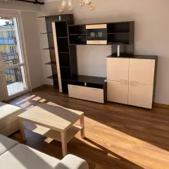 Jasne, nowoczesne mieszkania do wynajęcia Ostrołęka. Salon z meblościanką, stolikiem kawowym i kanapą. Duże okno z widokiem na balkon.