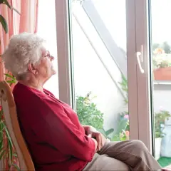 Starsza pani w czerwonym swetrze siedzi przy oknie, zastanawiając się, jak sprzedać mieszkanie z zameldowanym lokatorem.