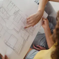 Dwie osoby analizują plan architektoniczny, omawiając, co to jest kondygnacja w budynku. Widoczne schody i pomieszczenia.
