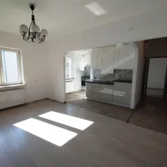 Jasne, nowoczesne mieszkania do wynajęcia Bytom. Widok na salon z oknem i kuchnię z białymi meblami.