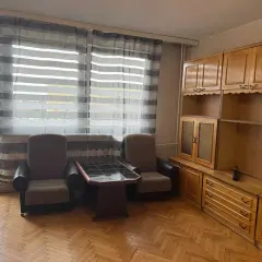 Przytulny salon z dwoma fotelami, stolikiem i drewnianą zabudową. Idealne mieszkania do wynajęcia Ciechanów.