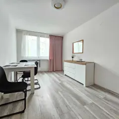 Jasne, nowoczesne mieszkania w Wodzisławiu Śląskim. Stół z krzesłami, komoda z lustrem i okno z różową zasłoną.
