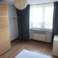 Przytulne mieszkanie do wynajęcia Gliwice. Jasny pokój z dużą szafą, oknem i białym meblem.