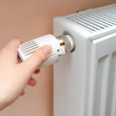 Ręka kręci termostatem grzejnika, przygotowując dom na zimę, kiedy włączają centralne ogrzewanie.