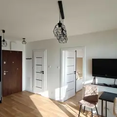 Nowoczesne mieszkania do wynajęcia Łomża. Jasne wnętrze z aneksem kuchennym, drzwiami i telewizorem.