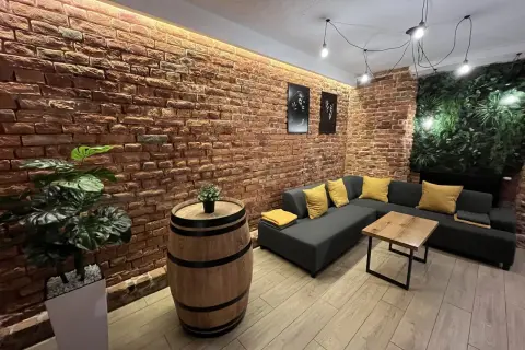 Nowoczesny lokal do wynajęcia Lublin. Ceglana ściana, wygodna kanapa, beczka jako stolik i zielona ściana.