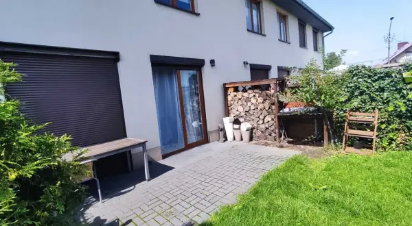 Taras przy domu w Rudzie Śląskiej, z drewnianą ławką, stertą drewna i zielonym ogrodem.