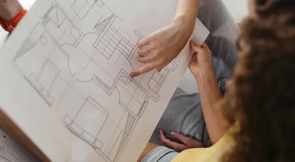Dwie osoby analizują plan architektoniczny, omawiając, co to jest kondygnacja w budynku. Widoczne schody i pomieszczenia.