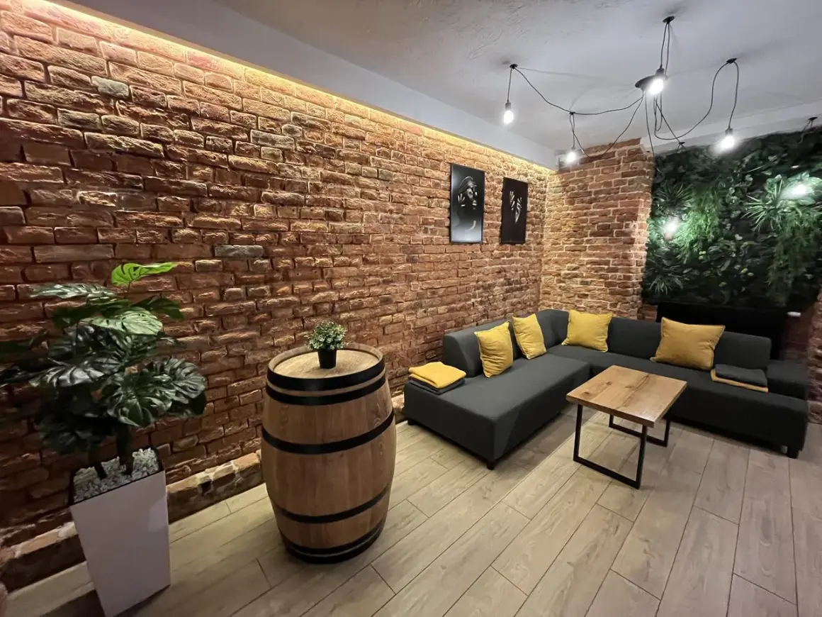 Nowoczesny lokal do wynajęcia Lublin. Ceglana ściana, wygodna kanapa, beczka jako stolik i zielona ściana.