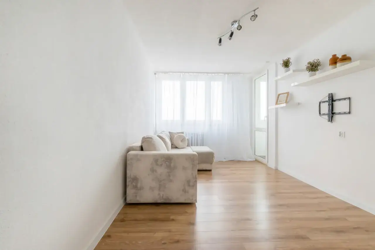 Jasny salon z beżową kanapą i drewnianą podłogą. Idealne miejsce na relaks. Pilnie sprzedam mieszkanie Toruń.