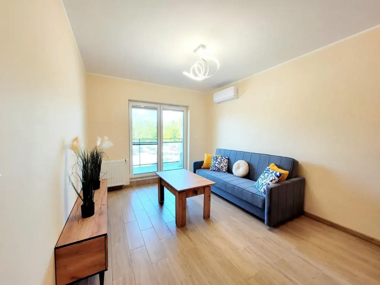Nowoczesne mieszkania do wynajęcia Ciechanów. Salon z wygodną kanapą, stolikiem i widokiem na balkon.