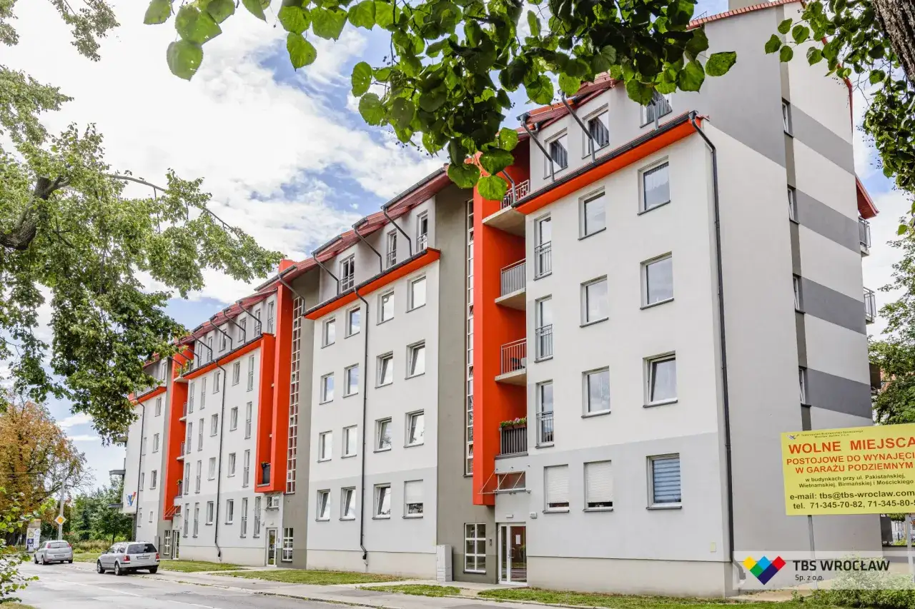 Nowoczesny budynek TBS Wrocław z pomarańczowymi akcentami. Wolne mieszkania i miejsca postojowe w garażu podziemnym.