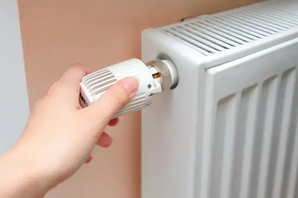Ręka kręci termostatem grzejnika, przygotowując dom na zimę, kiedy włączają centralne ogrzewanie.